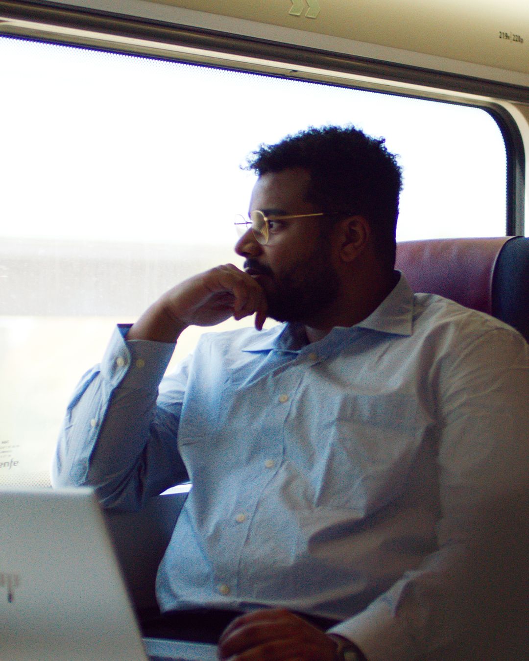 Un homme à lunettes regarde par la fenêtre du train, son ordinateur portable devant lui
